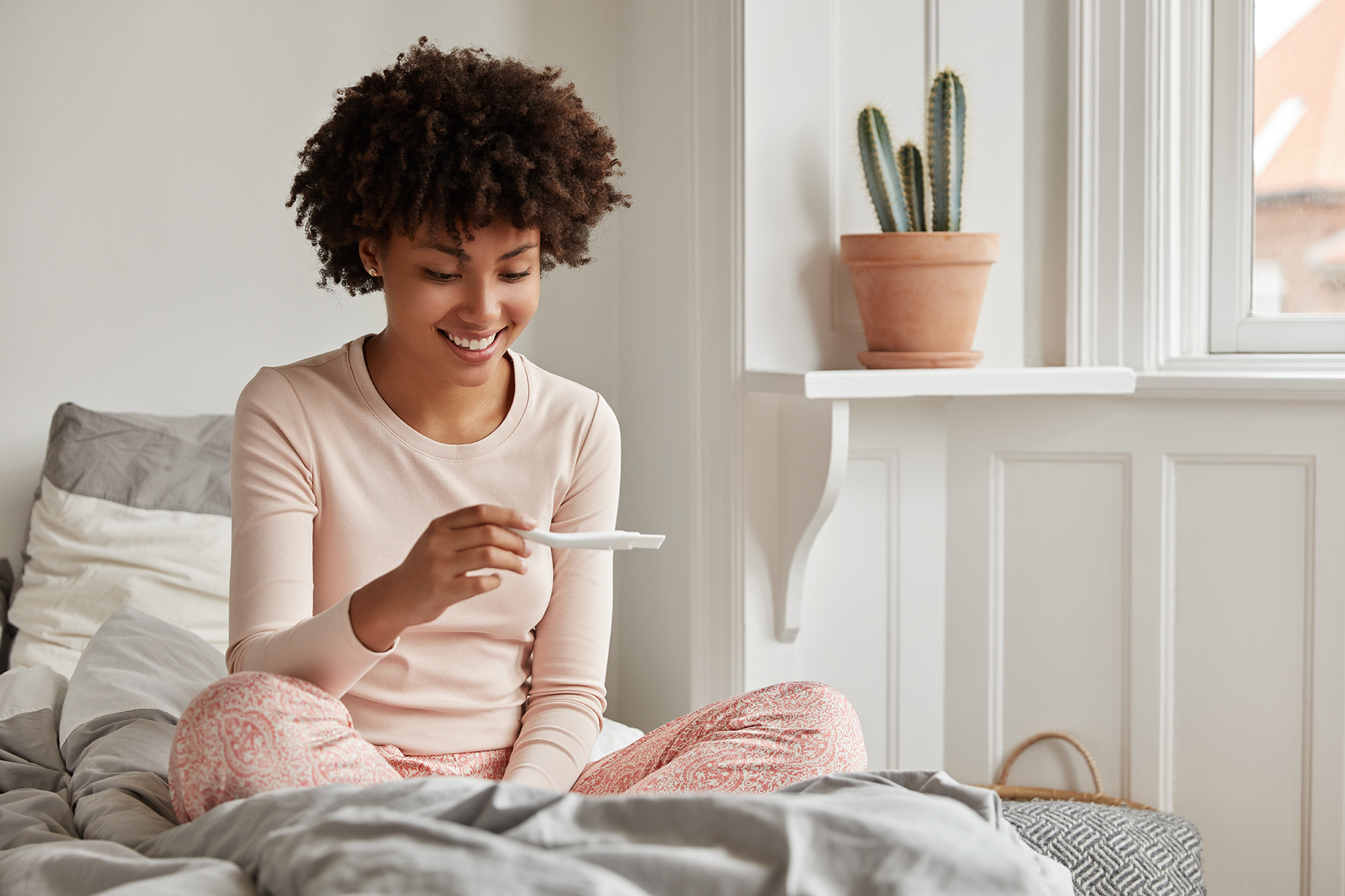 Young black woman sitting on bed in pajamas looking at pregnancy test Complete Healthcare Primary Care and Gynecology