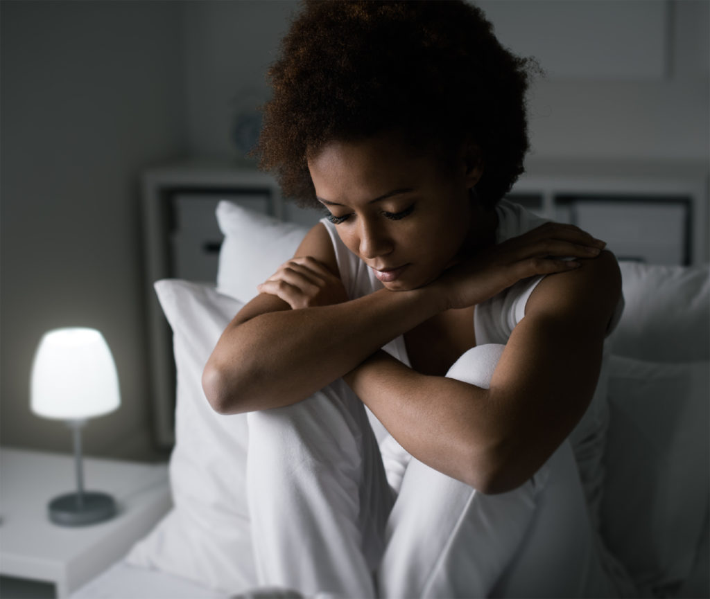 African american woman sitting alone on bed dealing with mental health issues Complete Healthcare Primary Care and Gynecology