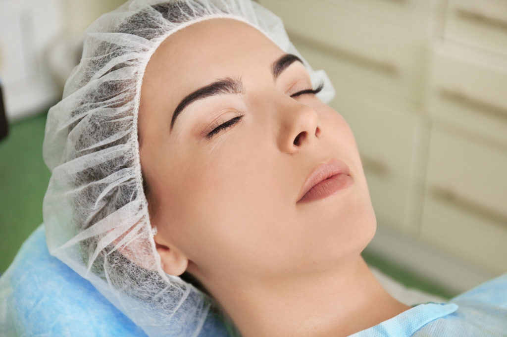 Young woman eyes closed with hairnet in doctors office waiting fro facial procedure Complete Healthcare Primary Care and Gynecology