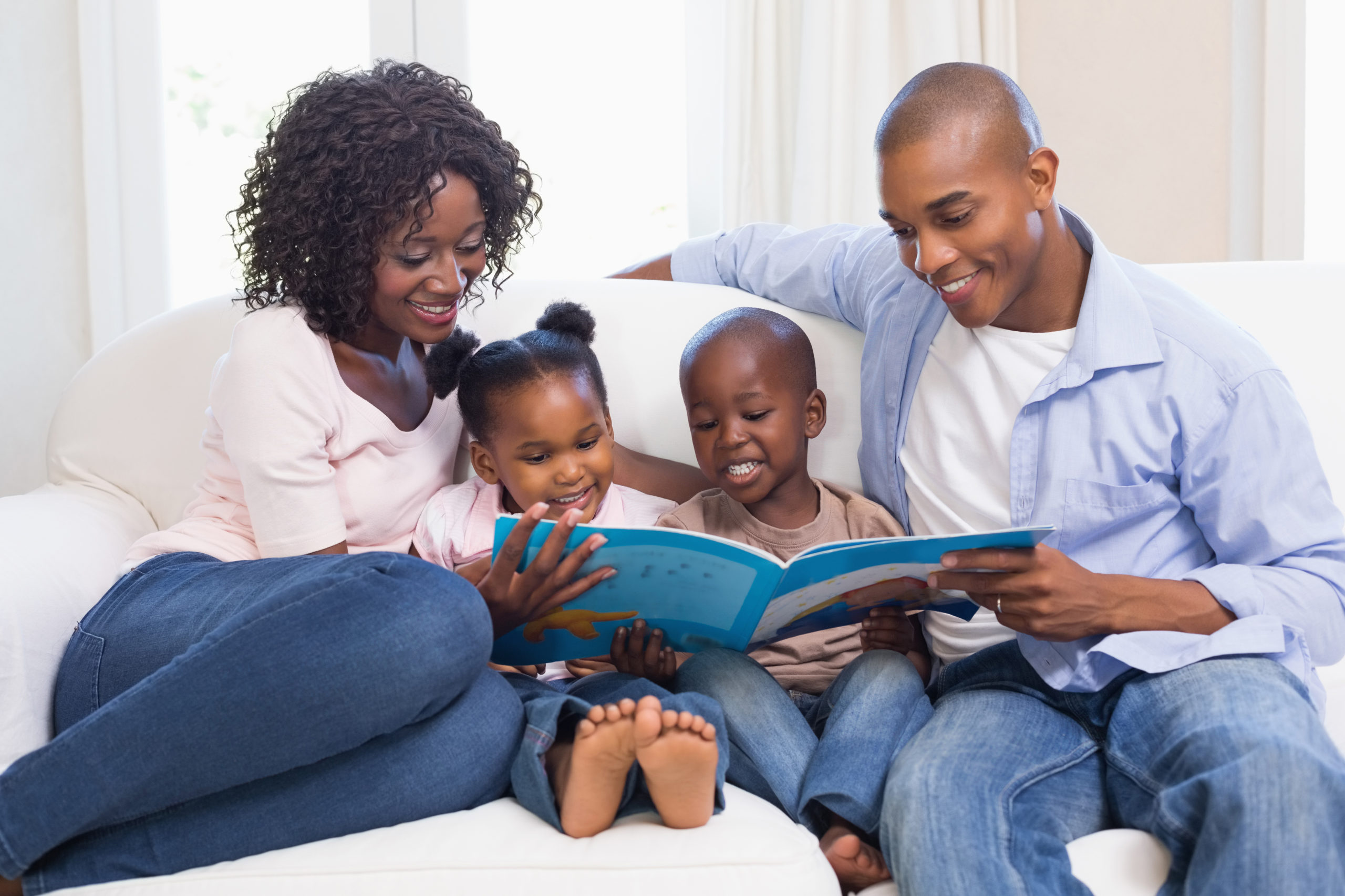 Black family on couch at home with their two children reading a storybook to them Complete Healthcare Primary Care and Gynecology