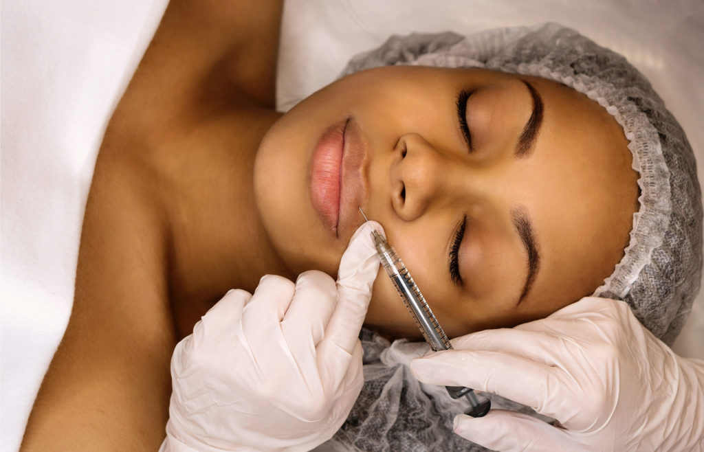 African african woman wearing hairnet at office getting injections in her lips from nurse Complete Healthcare Primary Care and Gynecology