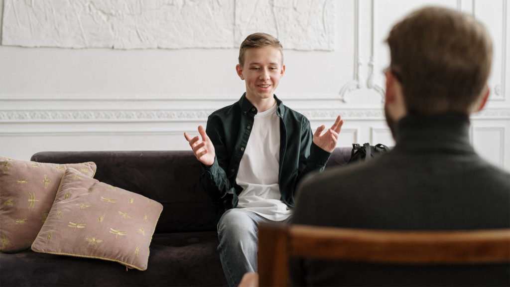 Young man sitting on couch and talking about mental health with counselor Complete Healthcare Primary Care and Gynecology