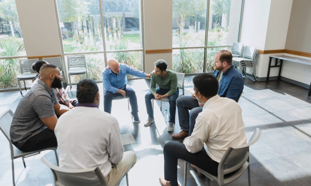 Men in addiction support group sitting in a circle in a well-lit room