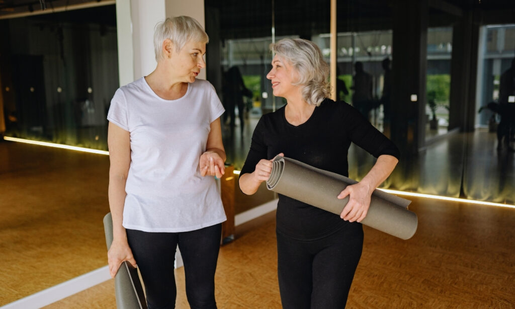 Older fit women at the gym holding tolled up yoga mats