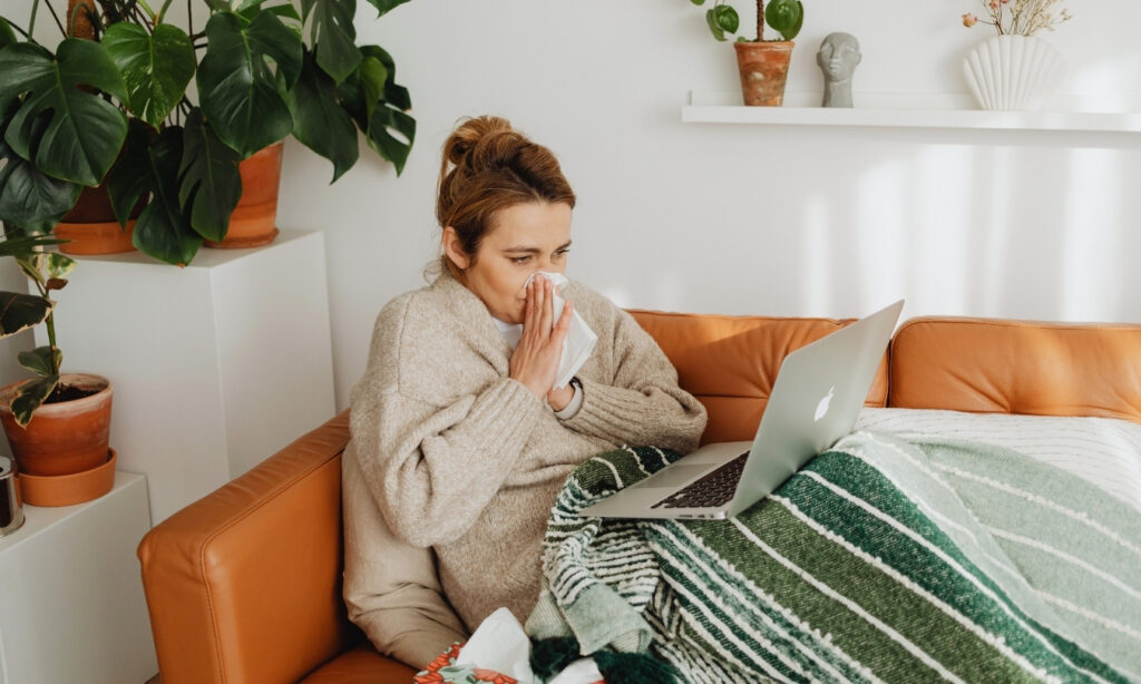 woman blowing her nose on the couch with a blanked