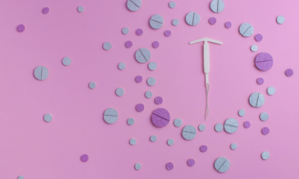 IUD surrounded by colorful pills against a pink background