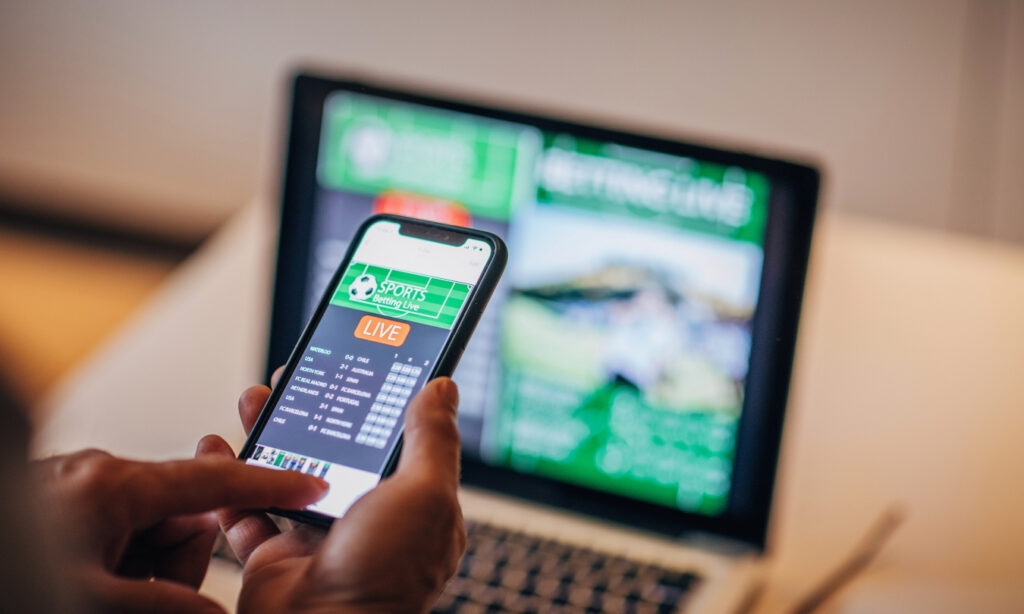 Person betting on sports using their phone and laptop