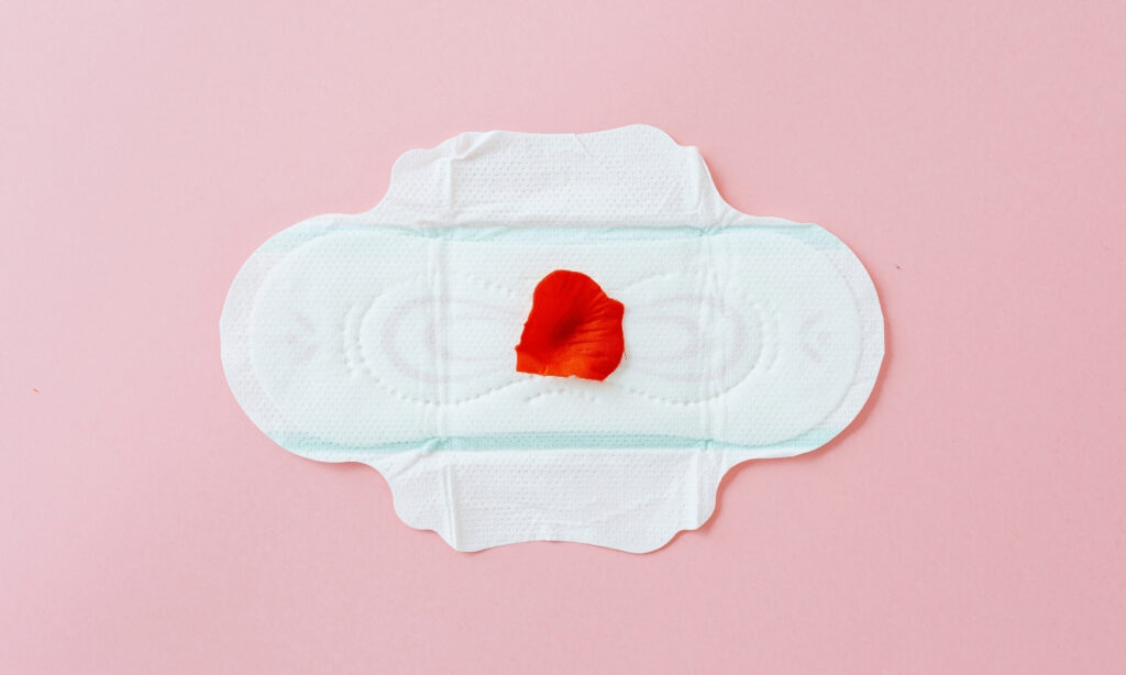Red flower petal placed in the middle of fresh menstrual pad against a light pink background