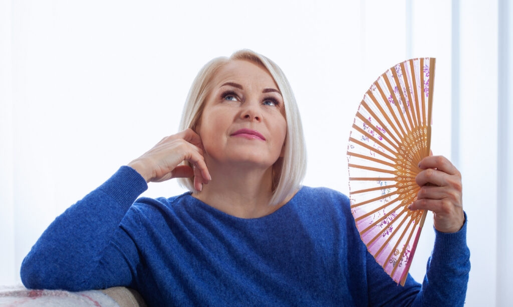 Older caucasian blonde woman fanning herself with a hand fan