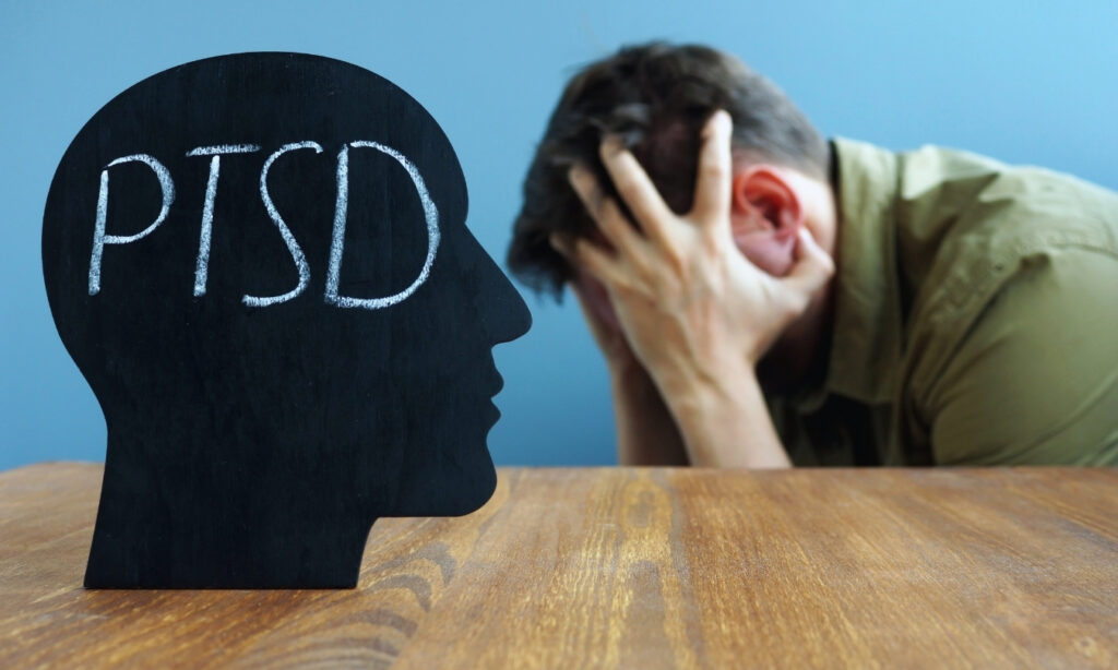 Man holding head in despair next to plastic cutout of a human head with"ptsd" written on it