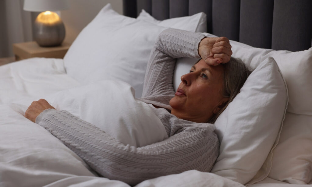 older blonde woman in bed experiencing a hot flash