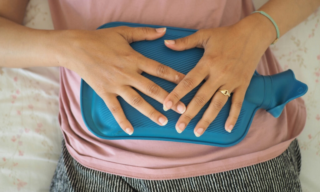 woman holding a hot pack to her stomach while lying down
